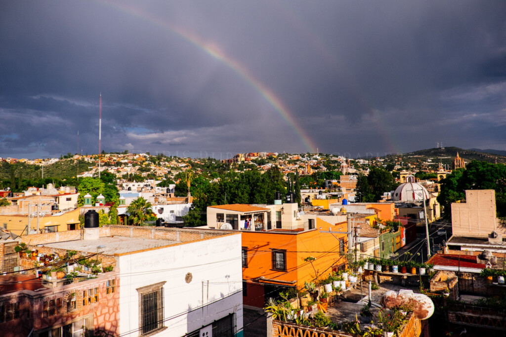 Rainbow arcing over the rooftops of San Miguel de Allende after a summer rainstorm, with the Parroquia de San Miguel Arcángel visible in the distance