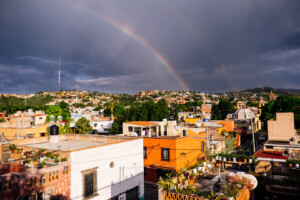 Rainbow arcing over the rooftops of San Miguel de Allende after a summer rainstorm, with the Parroquia de San Miguel Arcángel visible in the distance