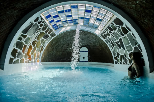 A visitor soaking beneath the waterfall spout in a domed, stained-glass thermal pool at Escondido Place hot springs