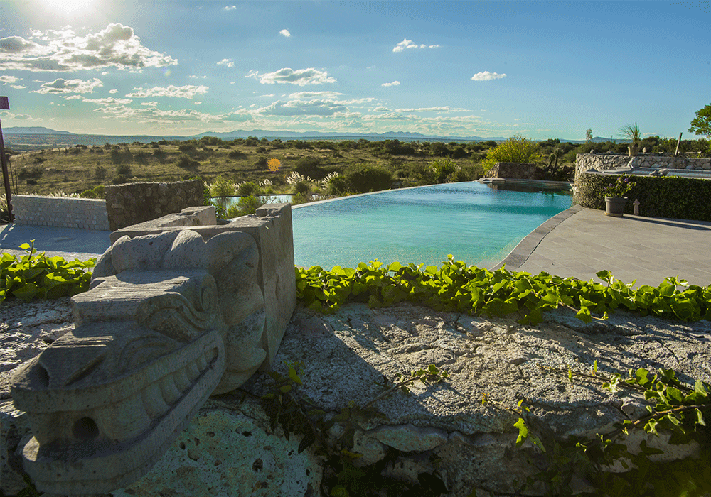The infinity pool at the Mayan Baths hot springs near San Miguel de Allende, with a carved feathered-serpent sculpture and countryside views