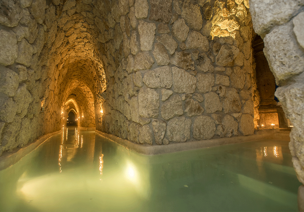 Candlelit underground stone tunnel filled with green thermal water at the Mayan Baths near San Miguel de Allende