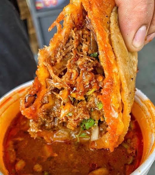 A quesabirria taco being dipped into rich consomé at Birria Barrio in Southtown, San Antonio