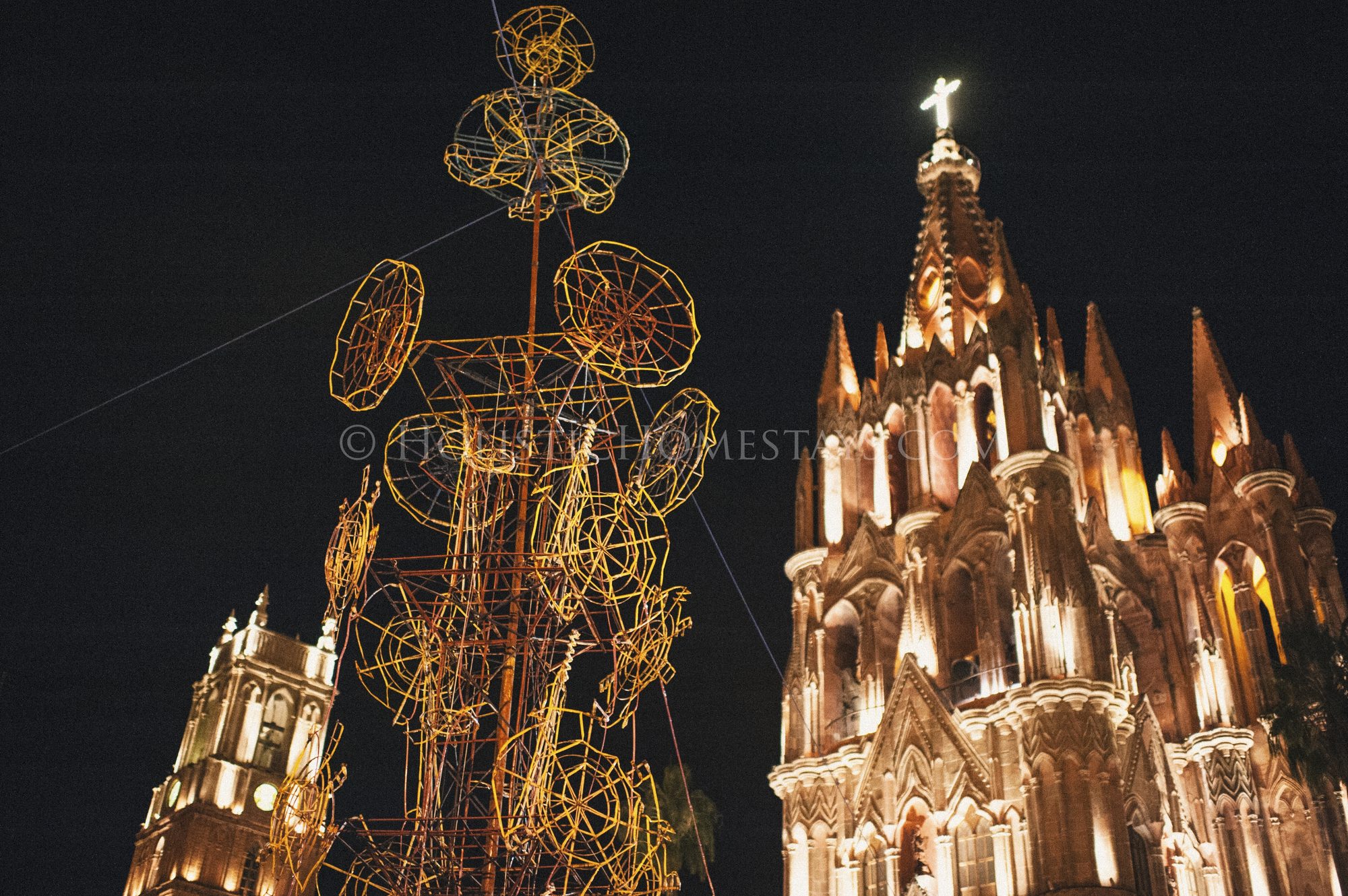 A castillo fireworks tower rigged with rockets and wheels standing beside La Parroquia at night in San Miguel de Allende