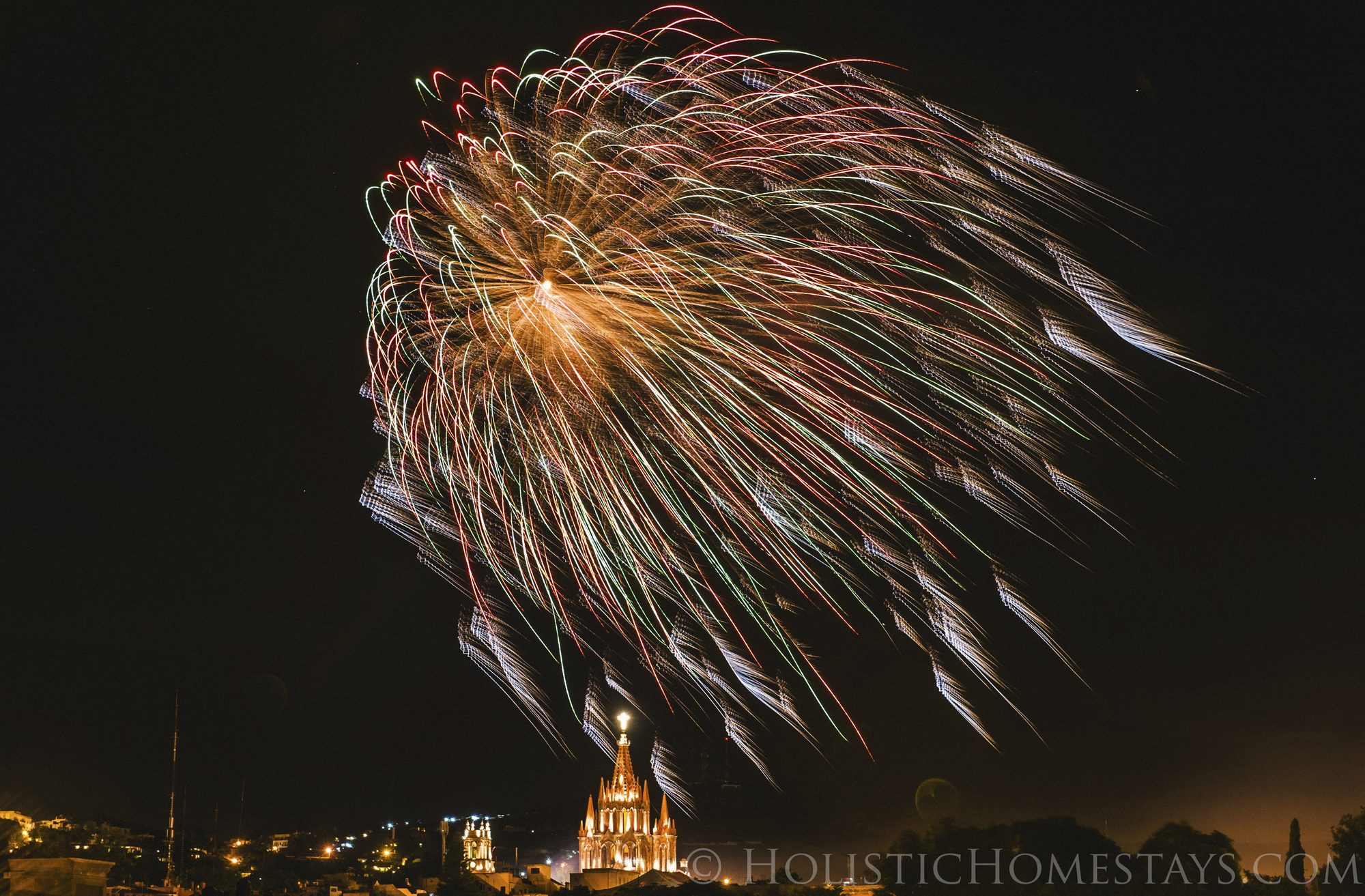 A large red and green fireworks burst above the spires of La Parroquia during San Miguel de Allende's September fiestas