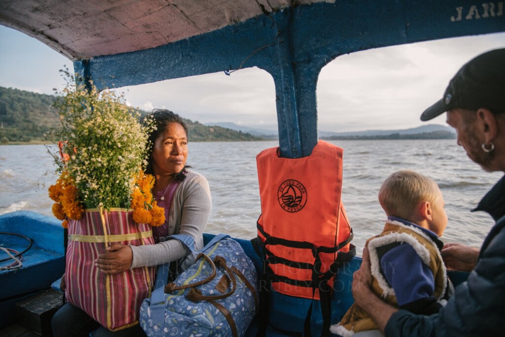 Family carrying flowers on a boat across Lake Pátzcuaro for Día de Muertos