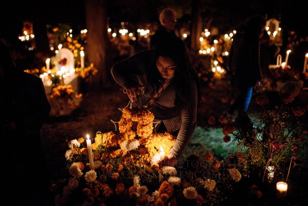 Woman lighting candles among marigolds at a family grave during Día de Muertos in the Lake Pátzcuaro region