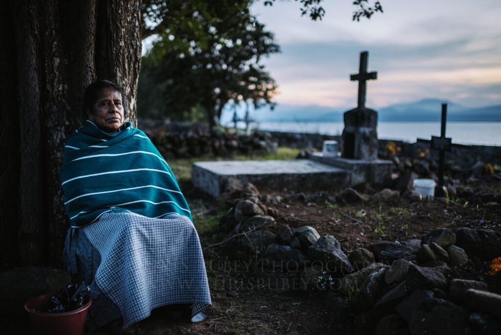 Woman wrapped in a rebozo waiting beside a family grave at dusk above Lake Pátzcuaro