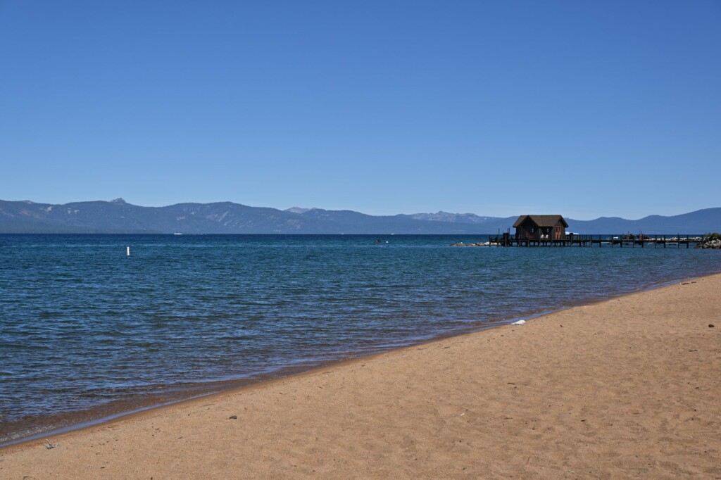 Coarse sand and calm blue water at Nevada Beach on Lake Tahoe, with a pier in the distance
