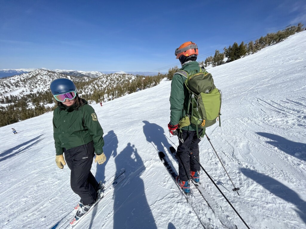 Two skiers on a groomed run at Heavenly with snowy mountains behind them